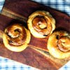 Three cinnamon rolls on a wooden cutting board with a blue and white checkered tablecloth.