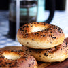 Stack of bagels with sesame seeds on a wooden surface, with a blurred coffee cup in the background.