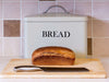 A loaf of bread with a knife and a bread box in the background
