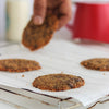 Freshly baked almond flour chocolate chip cookies on a cooling rack with a hand reaching for one, with a blurred background