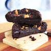 Sliced, fudgy Eggless Almond Fudge Brownie topped with roast almonds on a wooden board.