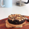 Freshly baked gluten free almond flour brownie topped with crushed almond praline on a wooden board.