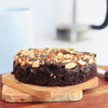 Freshly baked gluten free almond flour brownie topped with crushed almond praline on a wooden board.