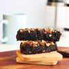 Freshly baked gluten free almond flour brownie topped with crushed almond praline on a wooden board.