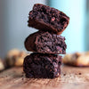 Stack of three chocolate brownies on a wooden surface with a blurred background