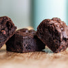 Close-up of three fudgy gluten free chocolate brownies on a wooden surface with a blurred background