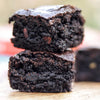 Two fudgy gluten free brownies stacked on a wooden surface with a blurred background
