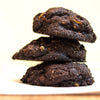 Stack of new york style chocolate almond praline cookies on a wooden surface with a blurred background