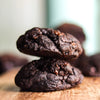 Stack of new york style dark chocolate chip cookies on a wooden surface with a blurred background
