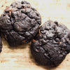 Two new york style dark chocolate chip cookies on a wooden surface