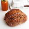 Classic Sourdough Country bread  with seeds on a white surface, next to a jar of jam and a knife.
