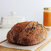 Classic Sourdough Country bread  with seeds on a white surface, next to a jar of jam and a knife.