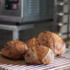 Freshly baked sourdough country loaves on a cooling rack with an oven in the background.