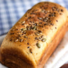 A close up of an Artisanal whole wheat sandwich bread with seeds on a wooden board with a blurred background