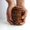 Stack of chocolate chip cookies held between two hands against a white background