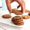 Hand picking a chocolate chip cookie from a stack of cookies on a cooling rack.