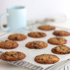 Freshly baked chocolate chip Cookies on a baking sheet with a blurred mug in the background