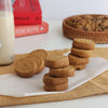 Stacks of round Jaggery Butter cookies on a white surface with a bottle of milk and a basket in the background.