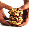 Stack of eggless New York Style Rum Raisin and Nut cookies held between two hands against a white background.