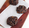 Three NYC Chocolate Almond Praline cookies on parchment paper on a wooden board
