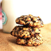 Stack of eggless New York Style Rum Raisin and Nut cookies with a glass of milk on a textured surface